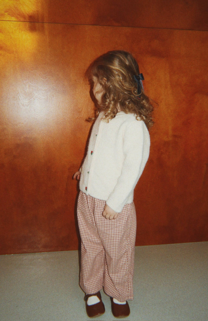 Barn i Foret Slit Pants och krämvit cardigan framför träpanel