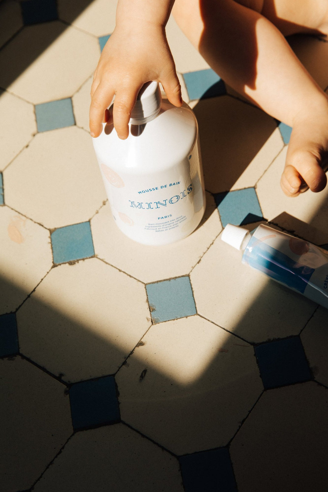 Barn som håller i flaskan med Bubble Bath på ett kaklat golv